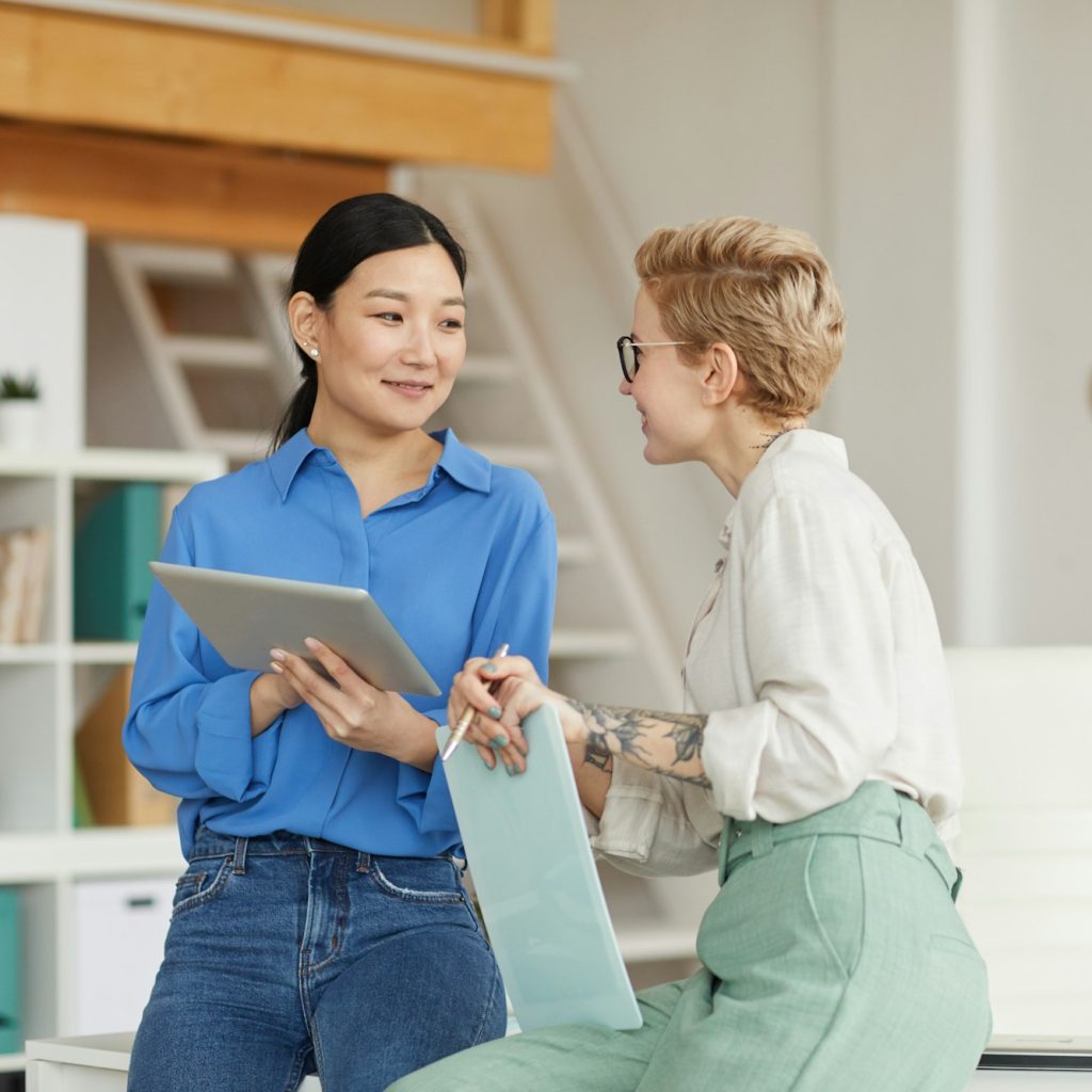 Two Smiling Businesswomen Communicating in Office